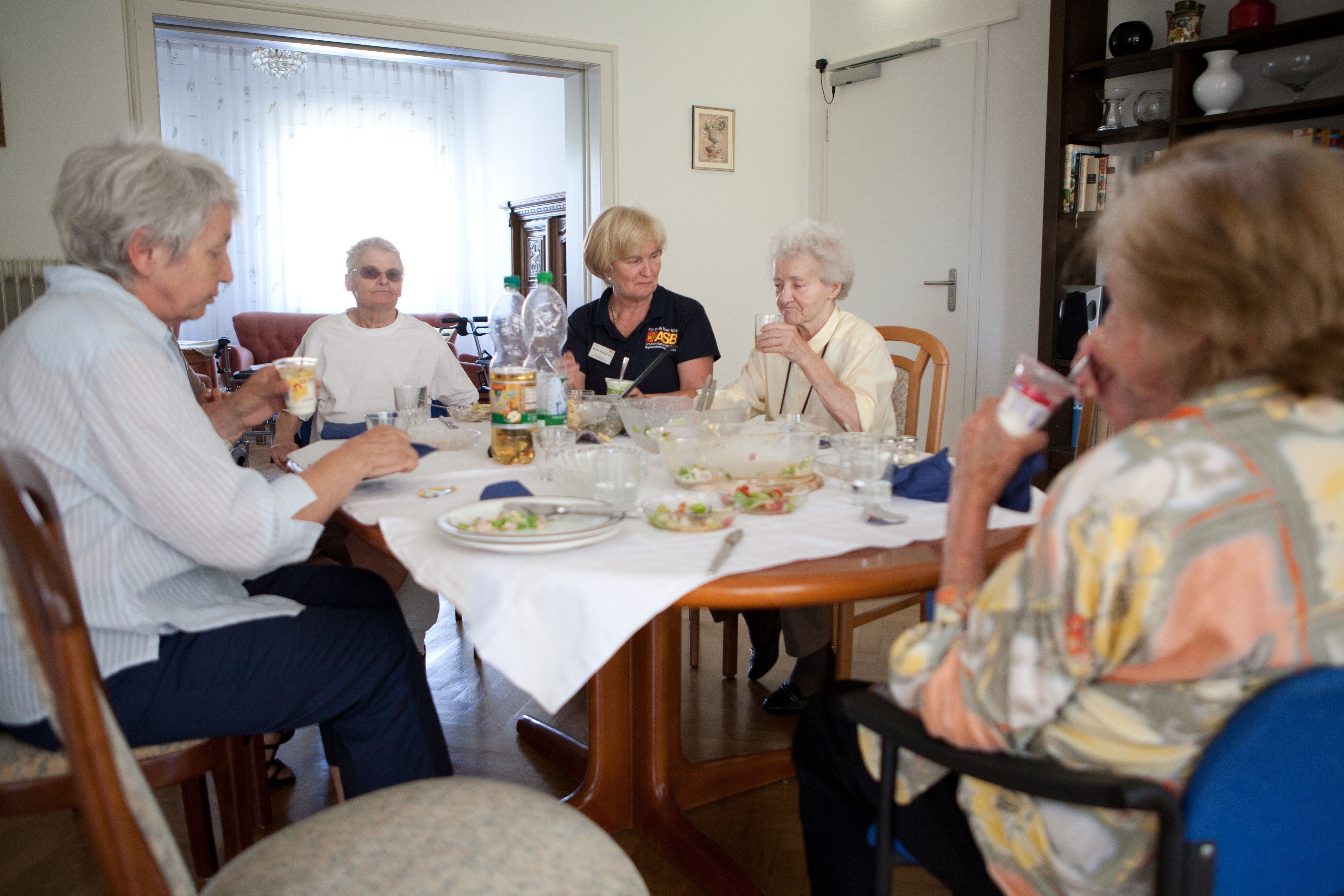 Mehrere Senioren sitzen gemeinsam im Esszimmer um einen großen Tisch beim Mittagessen.