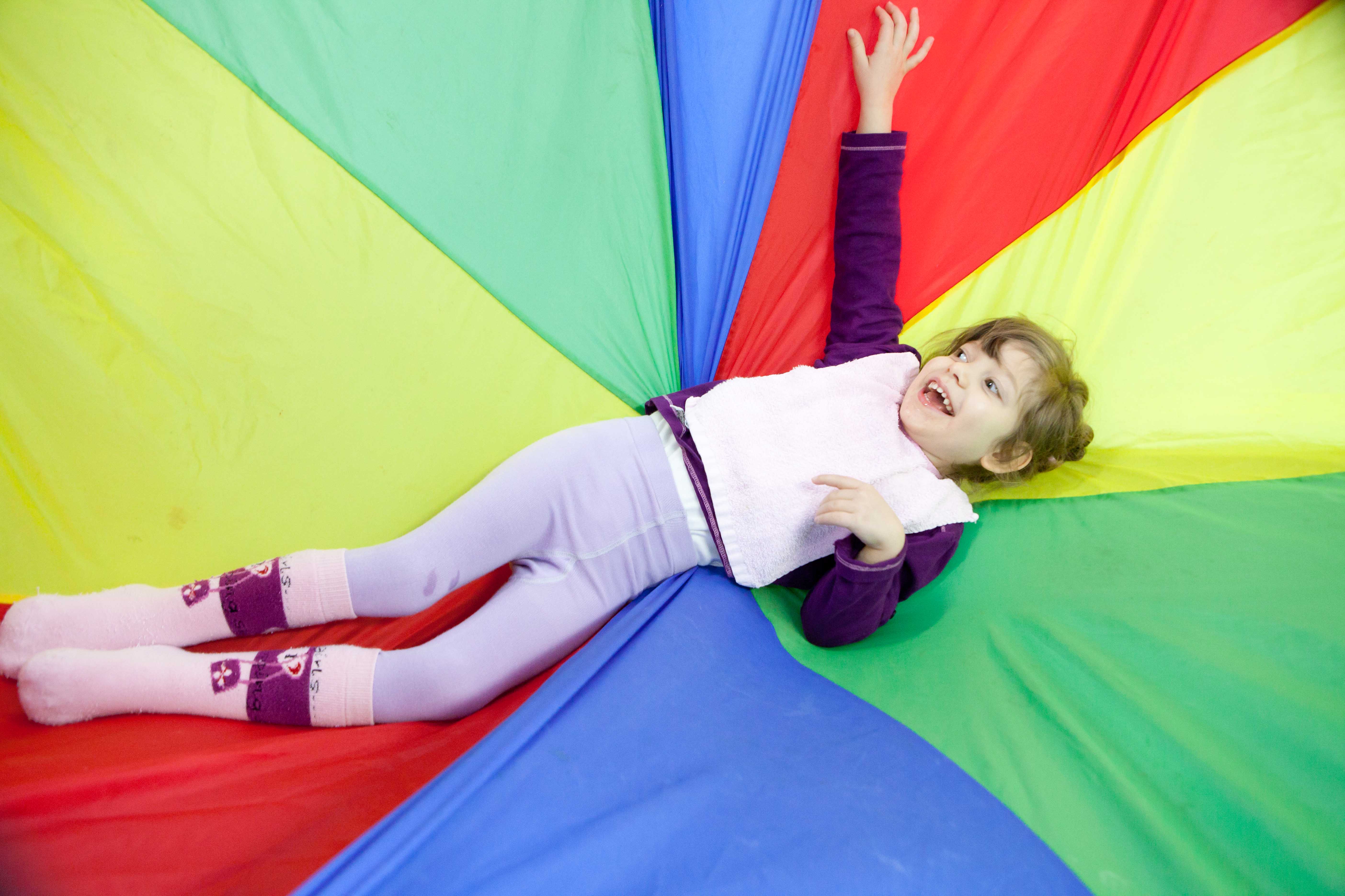 In einer integrativen Kindertagesstätte spielt ein Kind mit Beeinträchtigung mit bunten Tüchern