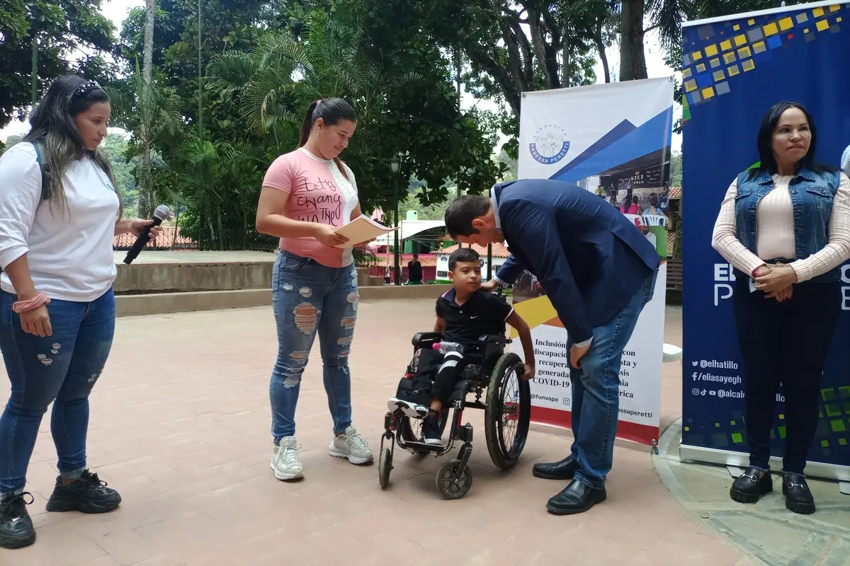 Ein Kind im Rollstuhl und seine Mutter unterhalten sich mit einem Verantwortlichen der Schule.