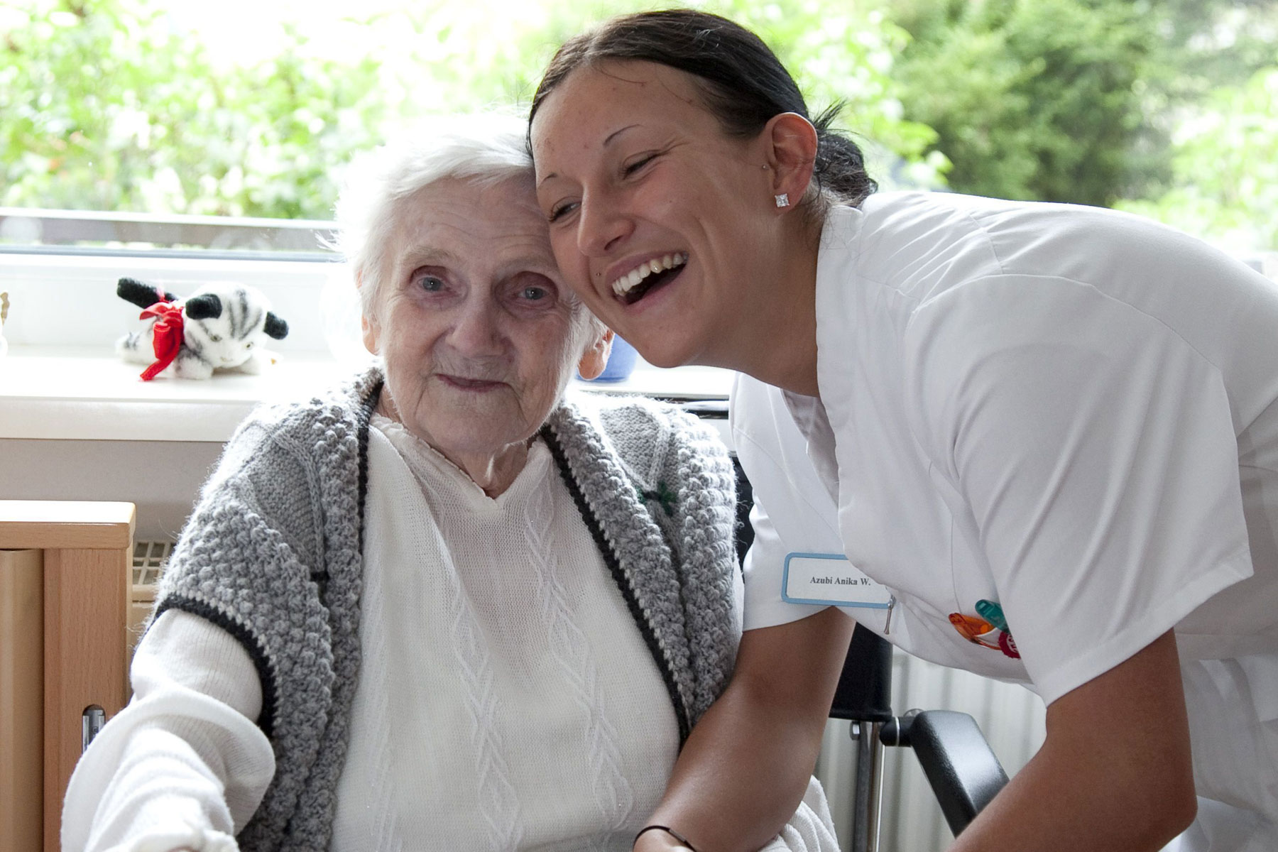 Kurzzeitpflege entlastet pflegende Angehörige Eine Pflegerin beugt sich zu einer alten Dame mit Rollator.