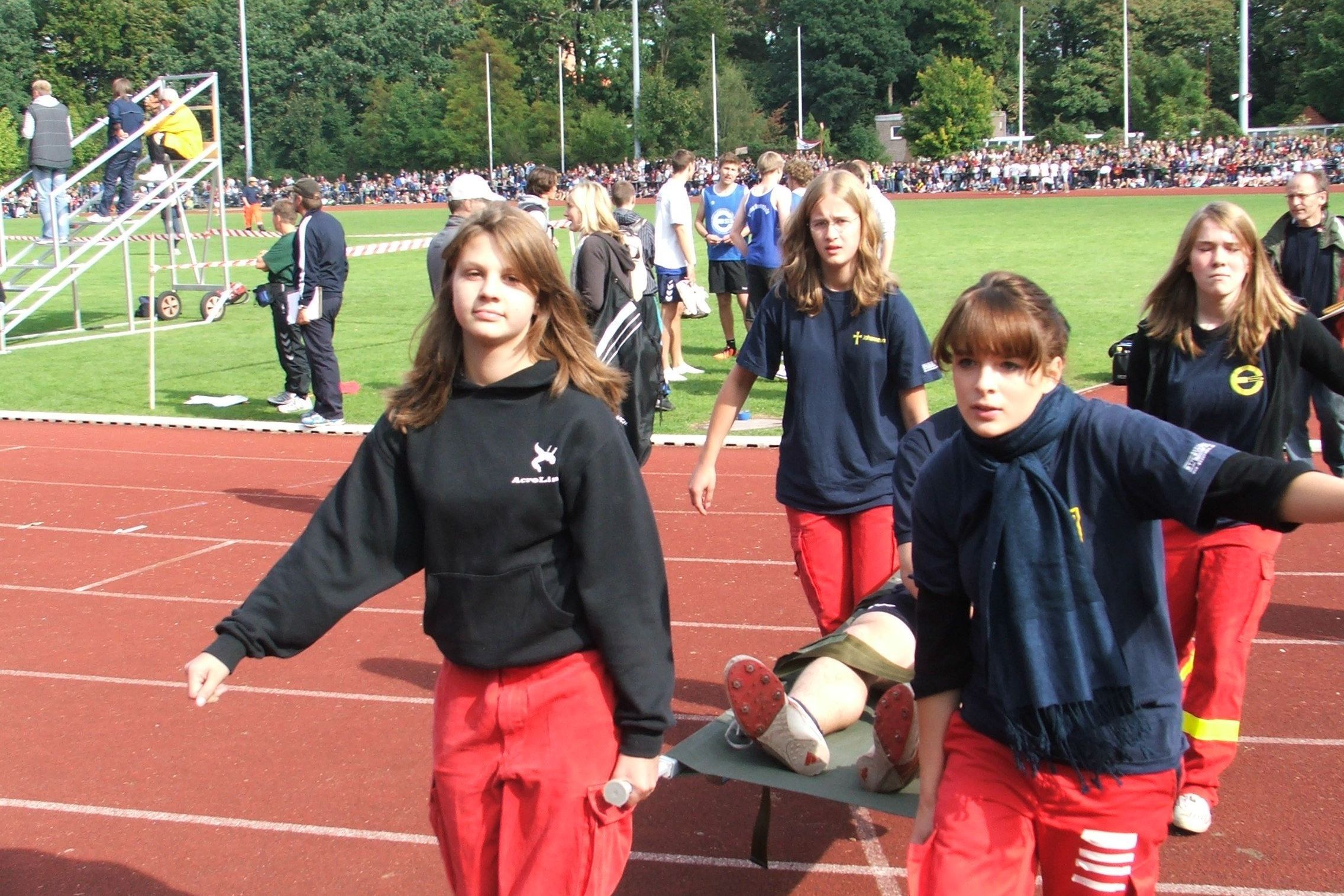 Vier Jugendliche tragen einen verletzten Mitschüler auf einer Trage vom Sportplatz.