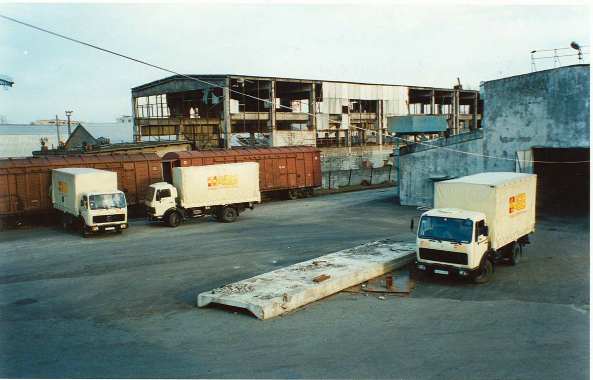 ASB-LKW stehen auf einem Industriegelände neben baufälligen Hallen in Poti. Im Hintergrund stehen Güterwaggons, die Nahrungsmittel geladen haben. (1996)